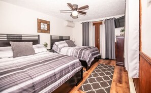 A bedroom with two beds, a ceiling fan, a rug, and a door leading to a bathroom.