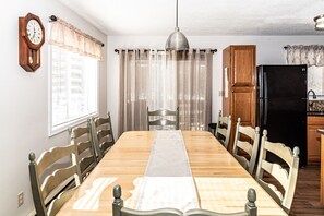 A dining room with a wooden table, chairs, a clock, and a refrigerator.
