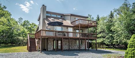 A two-story house with a stone facade, a wooden deck, and a covered entryway.