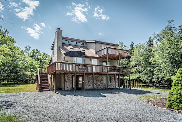 A two-story house with a stone facade, a wooden deck, and a covered entryway.