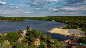 A lakeside property with a sandy beach, a parking area, and a small dock.