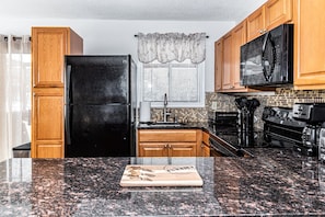 A kitchen with a black refrigerator, wooden cabinets, a microwave, and a tiled backsplash.