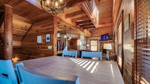 A wooden interior with a large dining table, blue chairs, and a chandelier.
