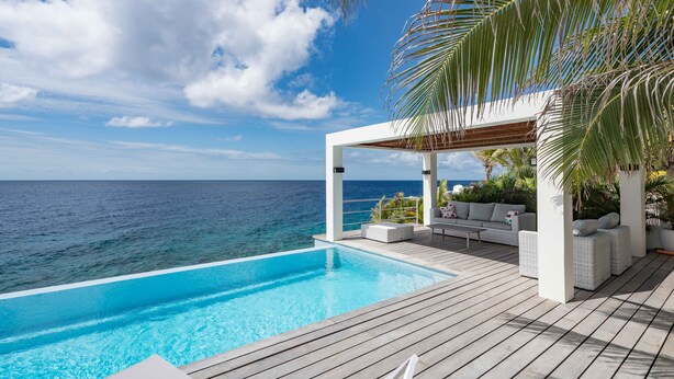 An infinity pool with a wooden deck, white outdoor furniture, and a view of the ocean. - Beautiful villa with breathtaking views and direct access to the sea (Rif St. Marie)
