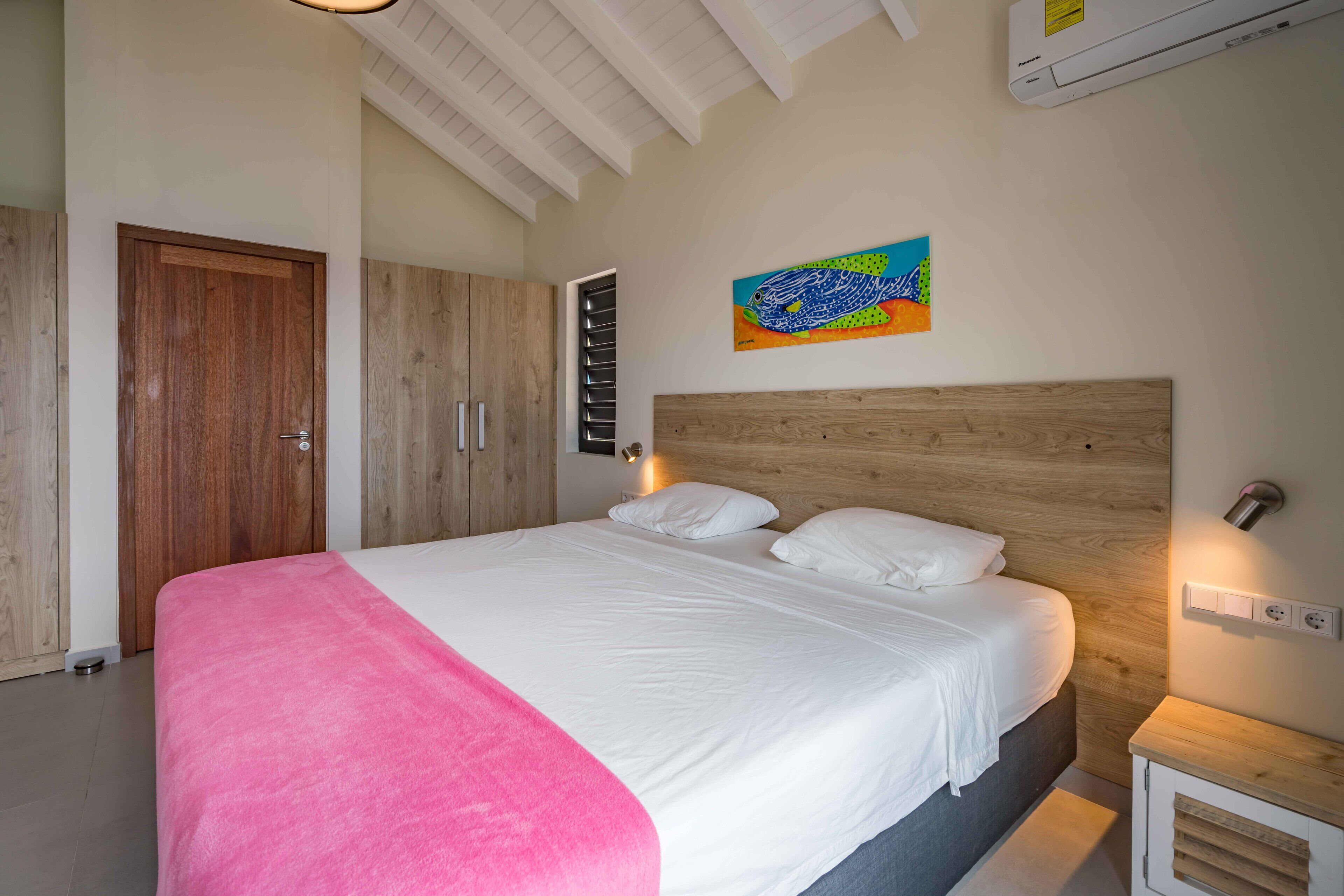 A bedroom with a large bed, wooden headboard, a painting on the wall, and a wooden wardrobe.
