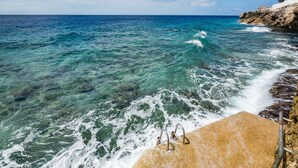 A beach with clear turquoise water, a rocky shoreline, and a concrete platform with metal handrails. - Beautiful villa with breathtaking views and direct access to the sea (Rif St. Marie)