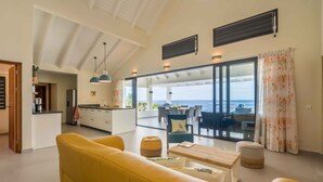A modern living room with a yellow sofa, a wooden coffee table, and a view of the sea through large glass doors. - Beautiful villa with breathtaking views and direct access to the sea (Rif St. Marie)