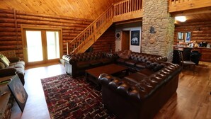 L’intérieur d’une cabane en rondins, avec un canapé d’angle en cuir, un escalier et un mur en pierre.
