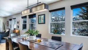 A dining area with a wooden table, chairs, a potted plant, and a view of snow-covered mountains through large windows. - Telemark Long Stay Condo: Perfect For 30 Days Or More (Breckenridge)
