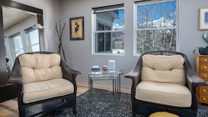 A living room with two wicker chairs, a glass coffee table, and a large window with a view of trees and a house. - Telemark Long Stay Condo: Perfect For 30 Days Or More (Breckenridge)