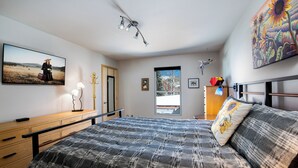A bedroom with a bed, a dresser, a desk, a window with a view, and a painting on the wall. - Telemark Long Stay Condo: Perfect For 30 Days Or More (Breckenridge)
