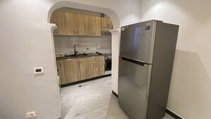 Moderni keittiö, jossa on vaaleat puukaapit, ruostumattomasta teräksestä valmistettu jääkaappi ja musta työtaso.