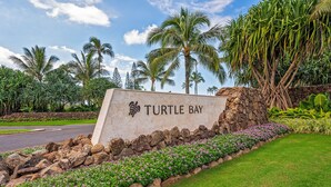 Letrero de Turtle Bay con un muro de piedra, césped verde y plantas tropicales.