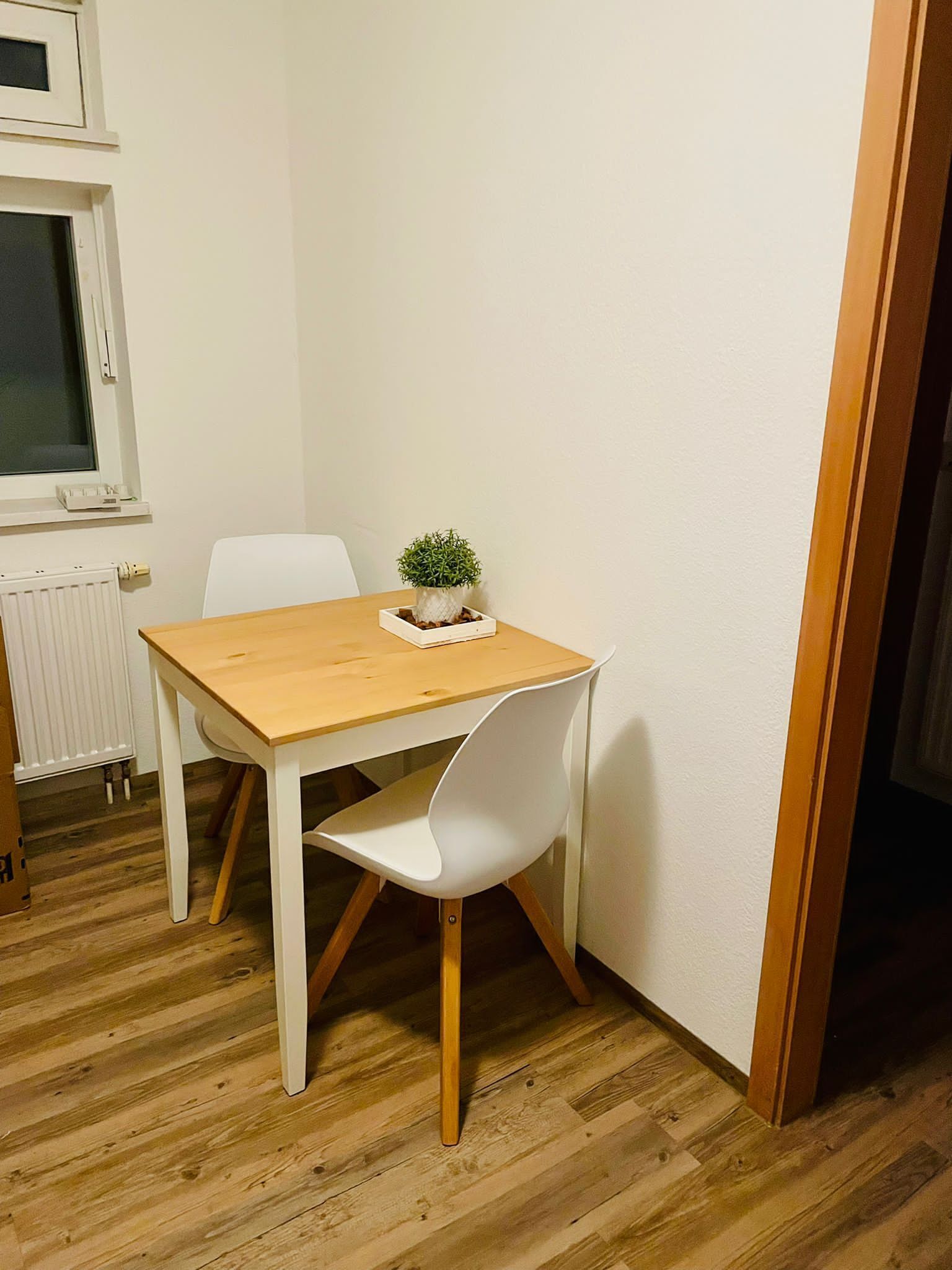 Ein kleiner Essbereich mit einem Holztisch und einem weißen Stuhl. Auf dem Tisch steht ein kleiner Blumentopf.