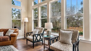 A room with large windows, a leather sofa, patterned chairs, and a floor lamp. - Bonavita ~ Come make memories, 5BR/5BA beach home! (Gulf Shores)