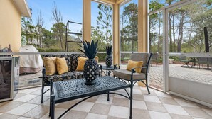 A covered patio area with a sofa, chairs, and a table, featuring a grill and potted plants. - Bonavita ~ Come make memories, 5BR/5BA beach home! (Gulf Shores)