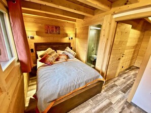 A wooden room with a bed, a window, and a door leading to another room.