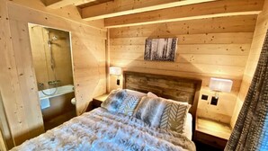 Camera da letto in una baita di legno, con un letto, comodini, uno specchio e un box doccia.