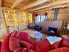 A cozy log cabin interior with a red sofa, a small round table, a fireplace, and a bookshelf filled with books and decorative items.
