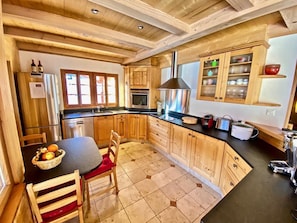 A kitchen with wooden cabinets, a black countertop, a stainless steel refrigerator, and a dining area with a table and chairs.