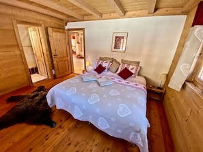 Ein Zimmer aus Holz mit einem Bett, einer Katze und einer Tür zu einem weiteren Raum.