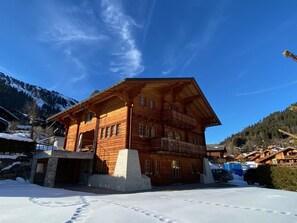 A wooden chalet with multiple balconies, a stone entrance, and a snowy landscape in the background.