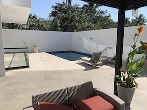 Un espace extérieur abrité comprenant une piscine, des chaises longues et un canapé en osier avec des coussins.