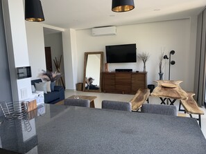 Un salon moderne avec un canapé gris, une table basse en bois et un téléviseur à écran plat fixé au mur.