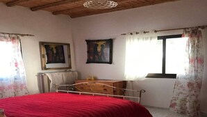 A bedroom with a metal bed frame, a red bedspread, a wooden dresser, and two framed pictures on the wall. - Rare and magical panoramic view of Mykonos and the Aegean sea. (Mikonos)