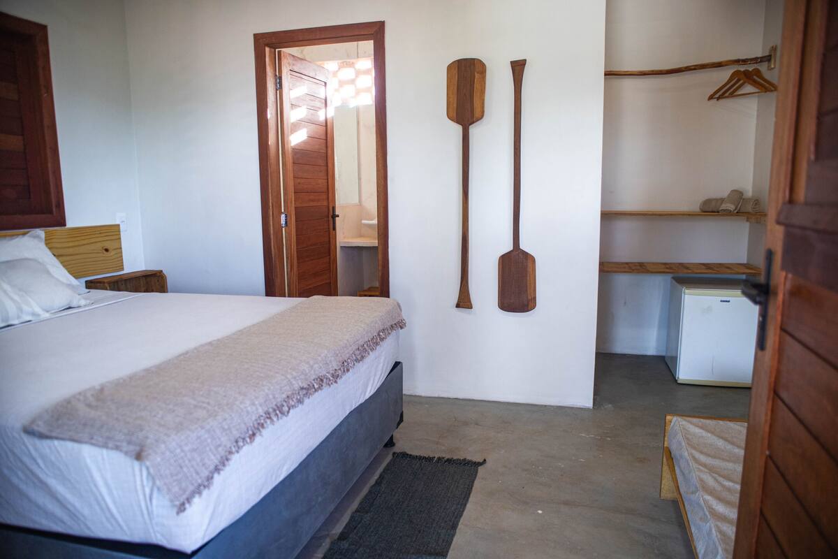 A bedroom with a bed, a wooden door, a small desk, and two wooden paddles on the wall.