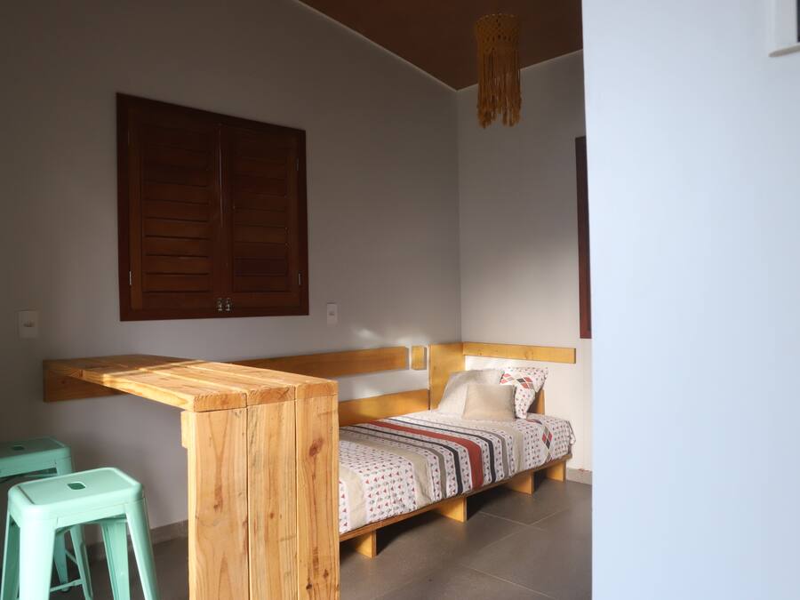 A single bed with a wooden headboard, a wooden bench, and two green stools.