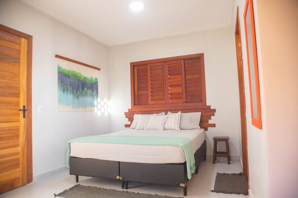 A bedroom with a bed, wooden headboard, a small stool, a rug, and a door.