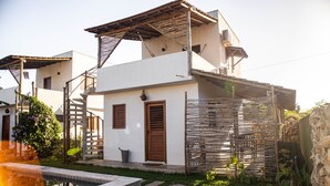Un edificio blanco con puerta de madera, un pequeño jardín y una piscina.