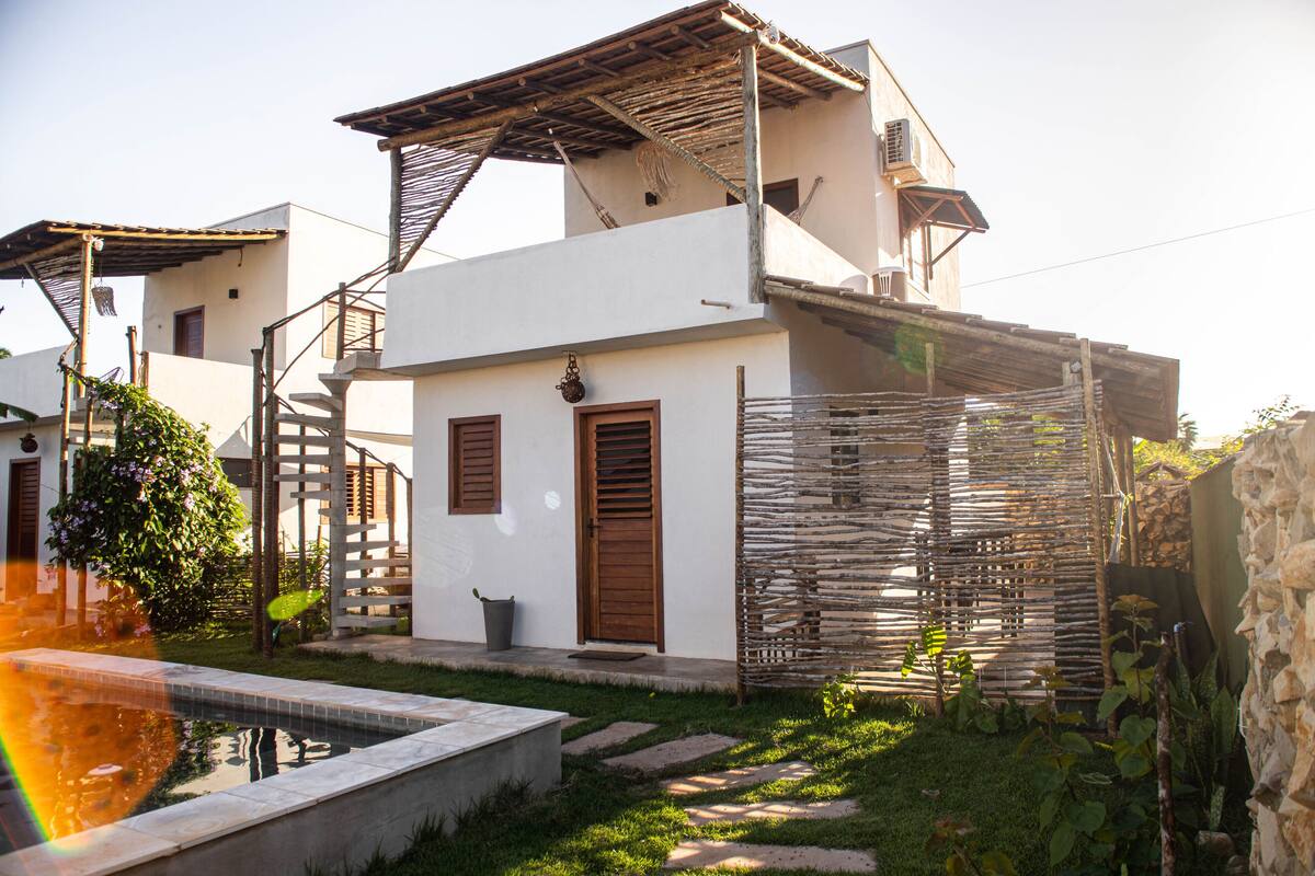 A white building with a wooden door, a small garden, and a pool.