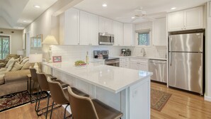 A modern kitchen with white cabinets, stainless steel appliances, and a central island with bar stools. - Community pool, dock, river views! (Kiawah Island)