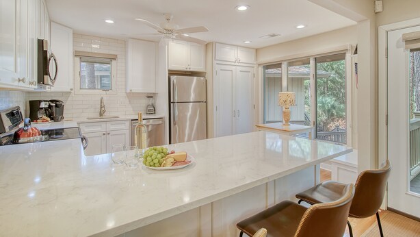 A modern kitchen with white cabinetry, a large island with a fruit bowl, and a view of the outdoors. - Community pool, dock, river views! (Kiawah Island)
