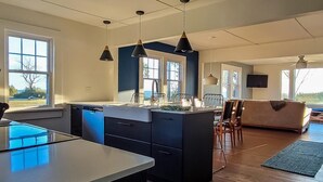 Une cuisine moderne dotée d’un îlot central, de luminaires suspendus et de grandes fenêtres.