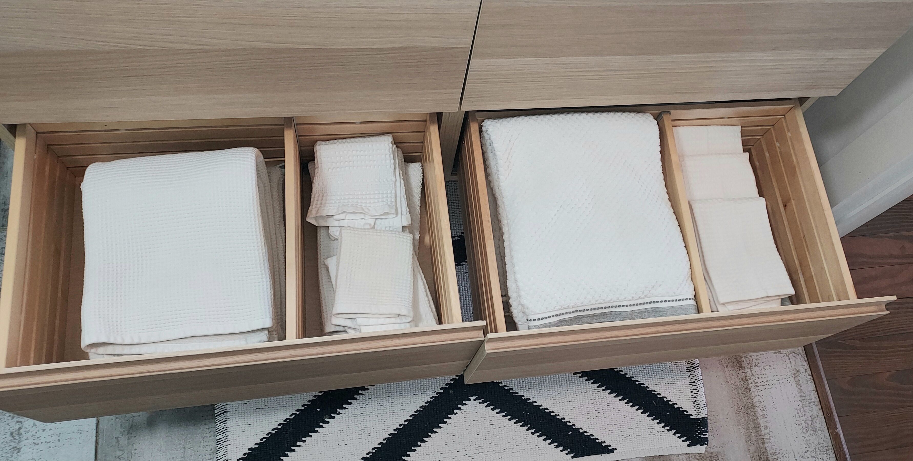 Un tiroir en bois doté de plusieurs compartiments, chacun contenant des serviettes blanches soigneusement pliées.