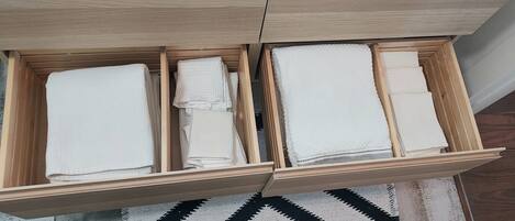 Un tiroir en bois doté de plusieurs compartiments, chacun contenant des serviettes blanches soigneusement pliées.