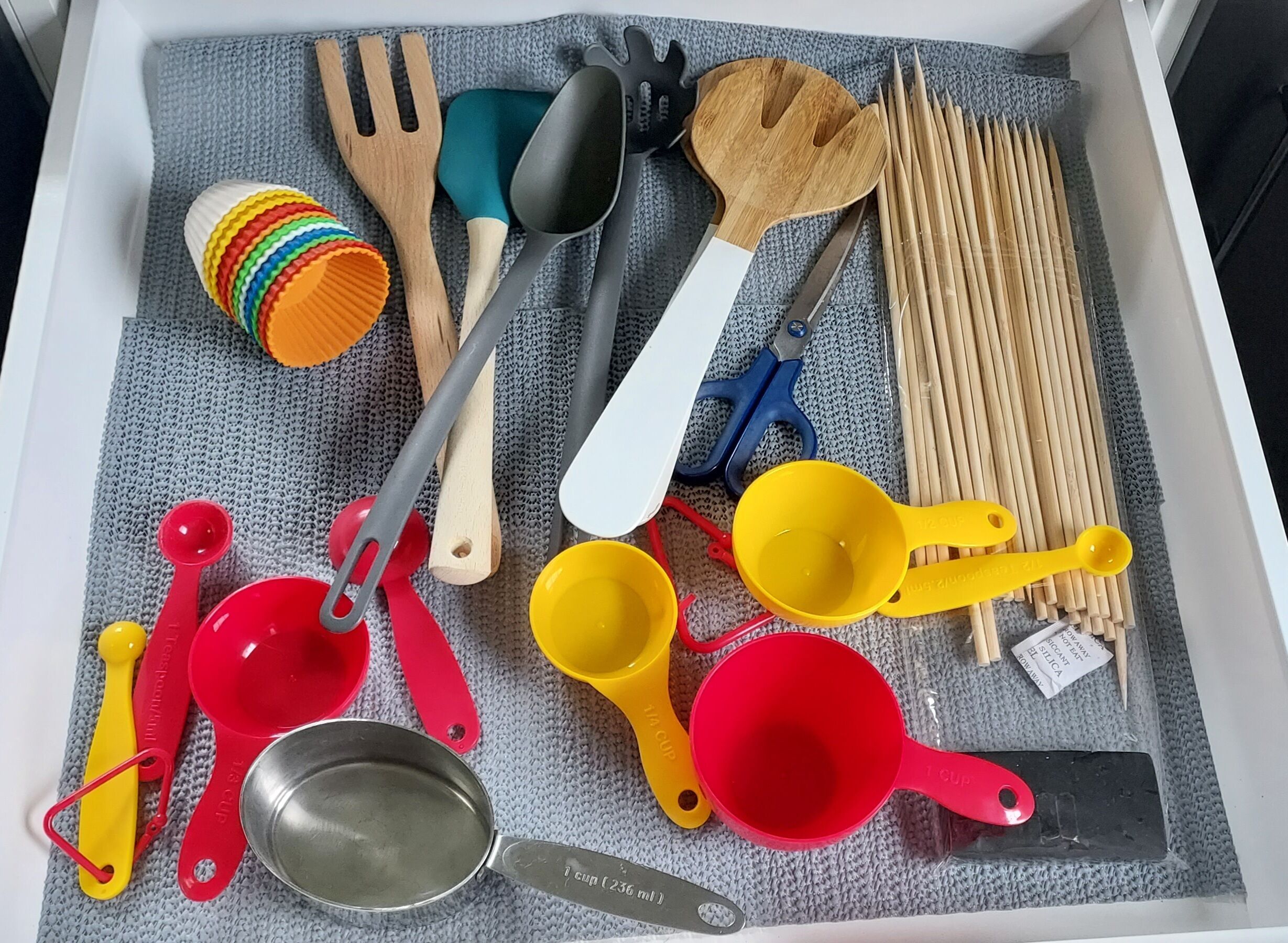 Un cajón con diversos utensilios de cocina, como tazas medidoras, cucharas y una espátula.