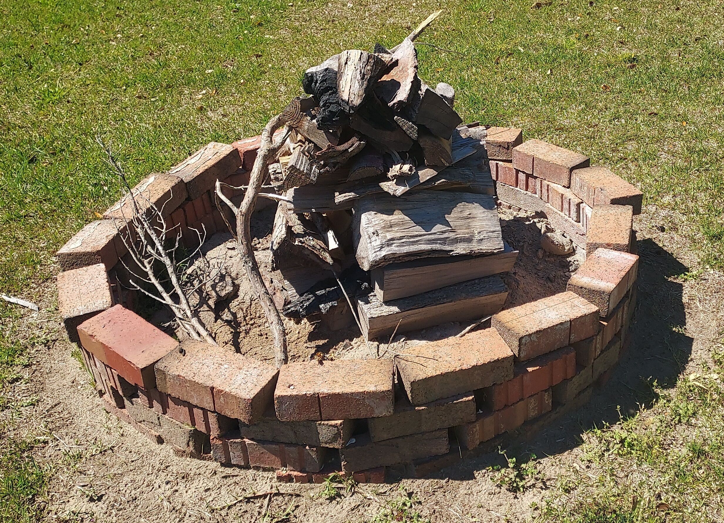 A circular brick fire pit with logs and a tree branch.