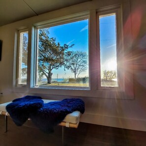 Ein Zimmer mit großem Fenster und Blick auf Bäume und ein Gewässer.