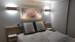 A modern bedroom with a bed, two pillows, a nightstand, a wall-mounted light, and a painting. - Haven of peace with garden and view - au Bouillat d'Anty (Châtel-Guyon)