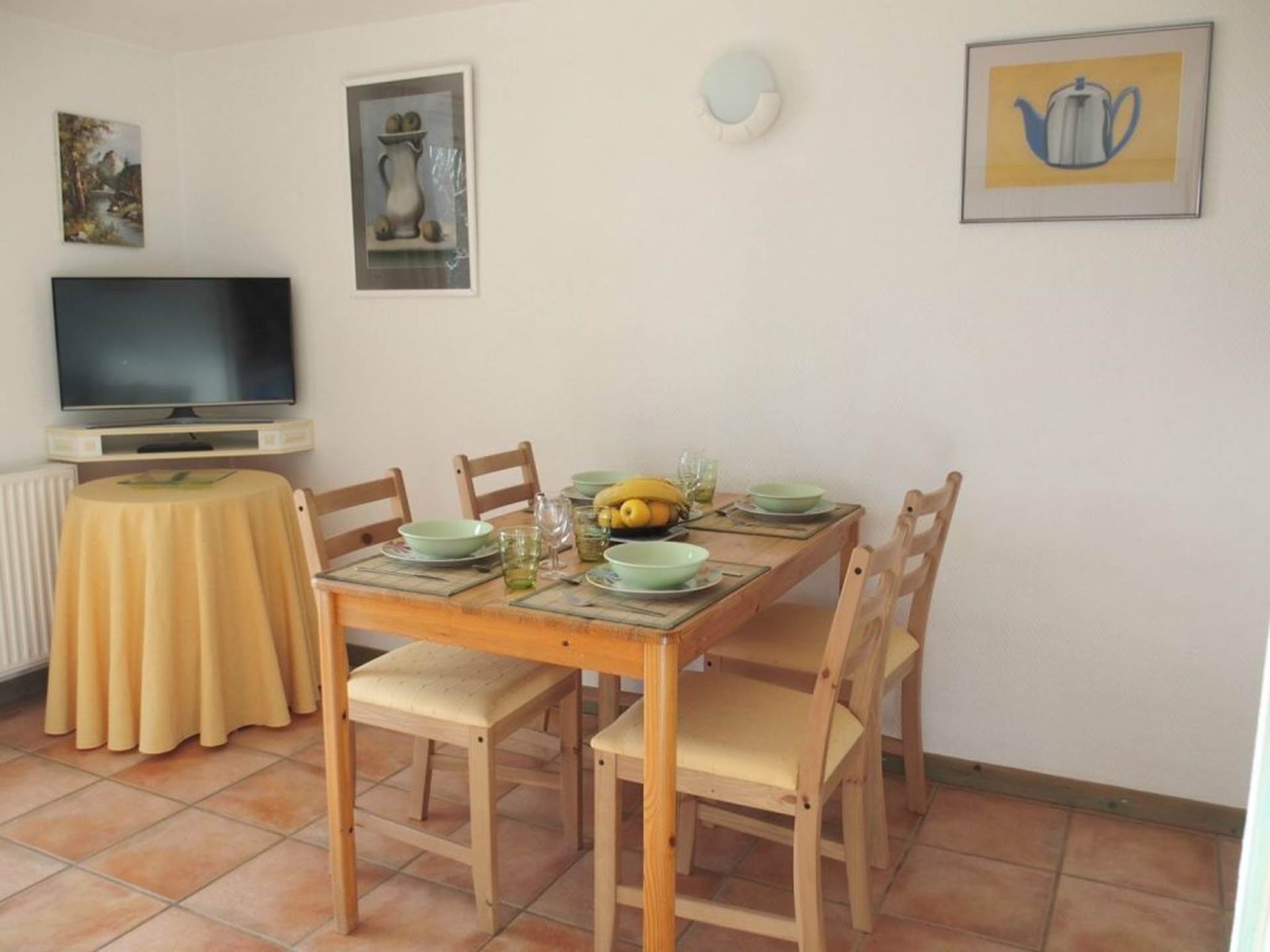A dining area with a wooden table, four chairs, and a television on a stand.