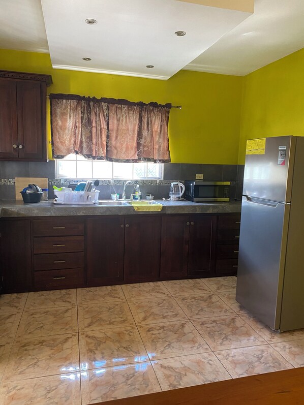 A kitchen with dark wooden cabinets, a stainless steel refrigerator, a microwave, and a sink with a faucet.