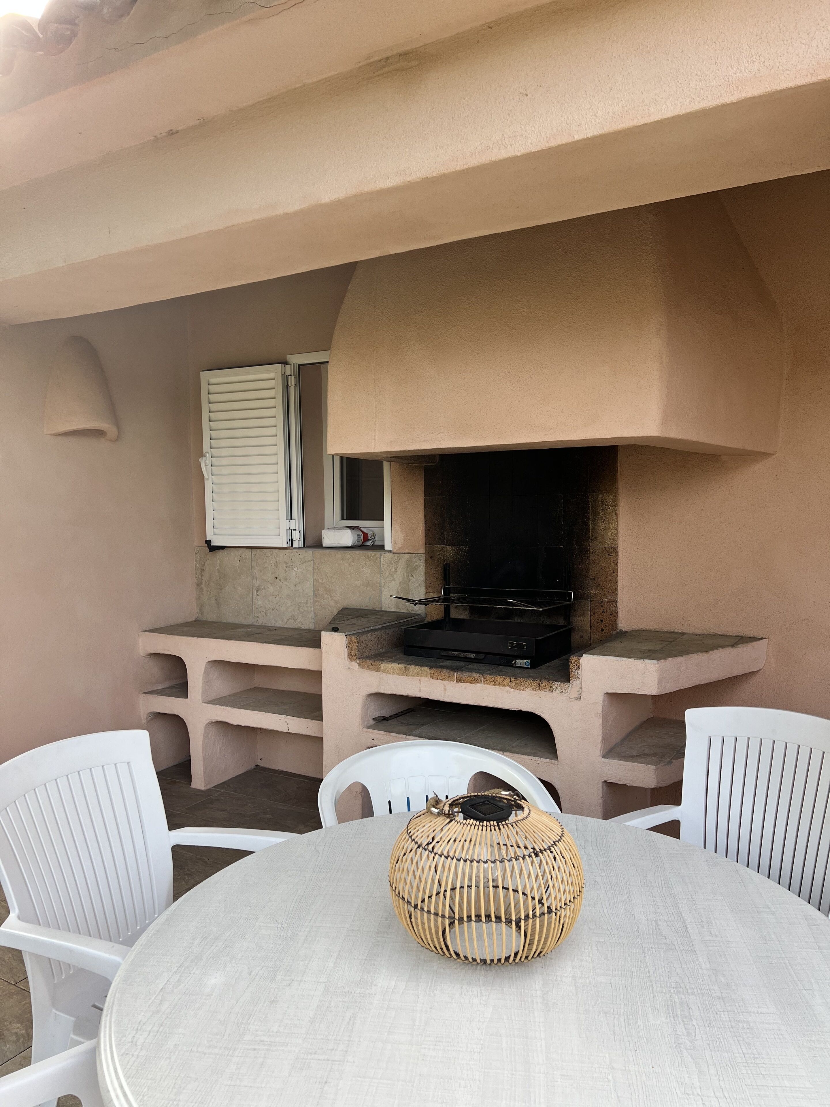An outdoor patio with a built-in grill, white chairs, and a woven basket on the table.