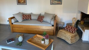 Een gezellige woonkamer met een houten bank, twee ingelijste kunstwerken, een klein bijzettafeltje, een geweven stoel en een dienblad met decoratieve items.