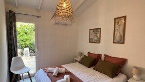 Een netjes opgemaakt bed met een bruine deken, een witte stoel en een hangende lamp.