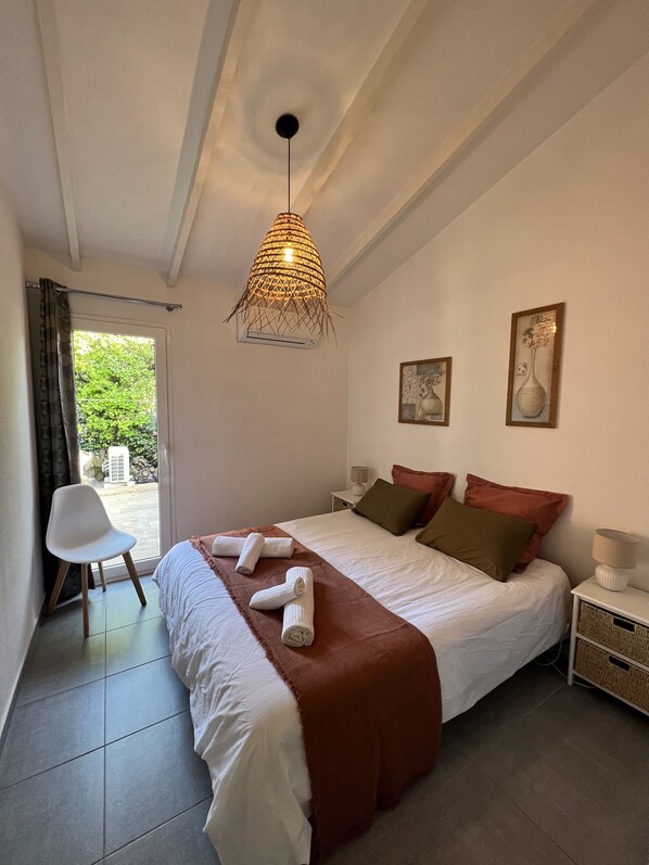 A neatly made bed with a brown blanket, a white chair, and a hanging light fixture.