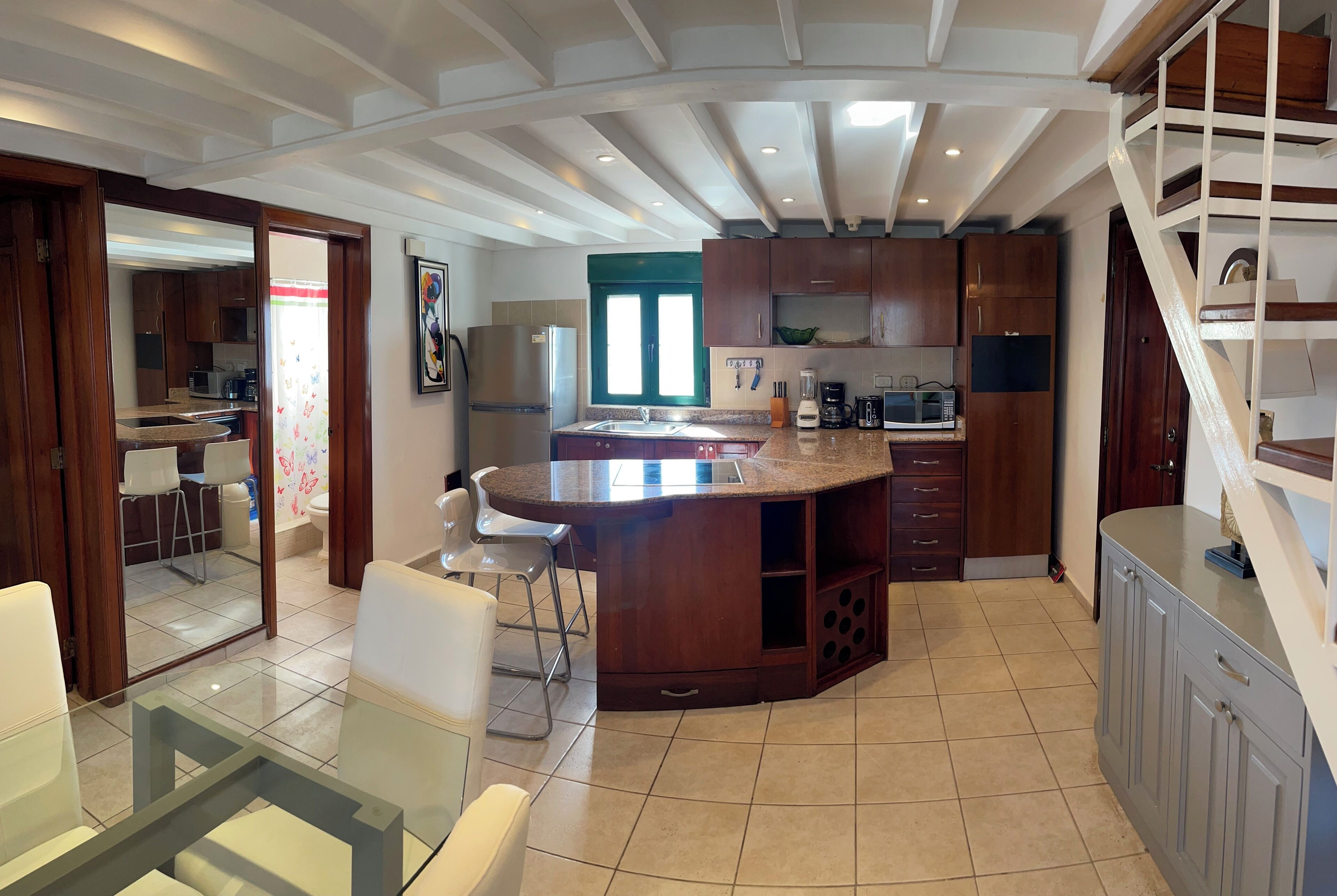 Una cocina moderna con una isla central, armarios de madera y un comedor con sillas blancas.